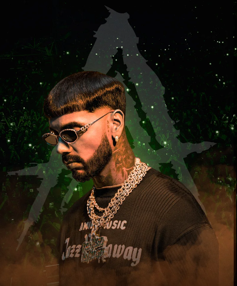 Anuel AA con gafas, cadenas y camiseta oscura, frente al público y la A de Real Hasta La Muerte.