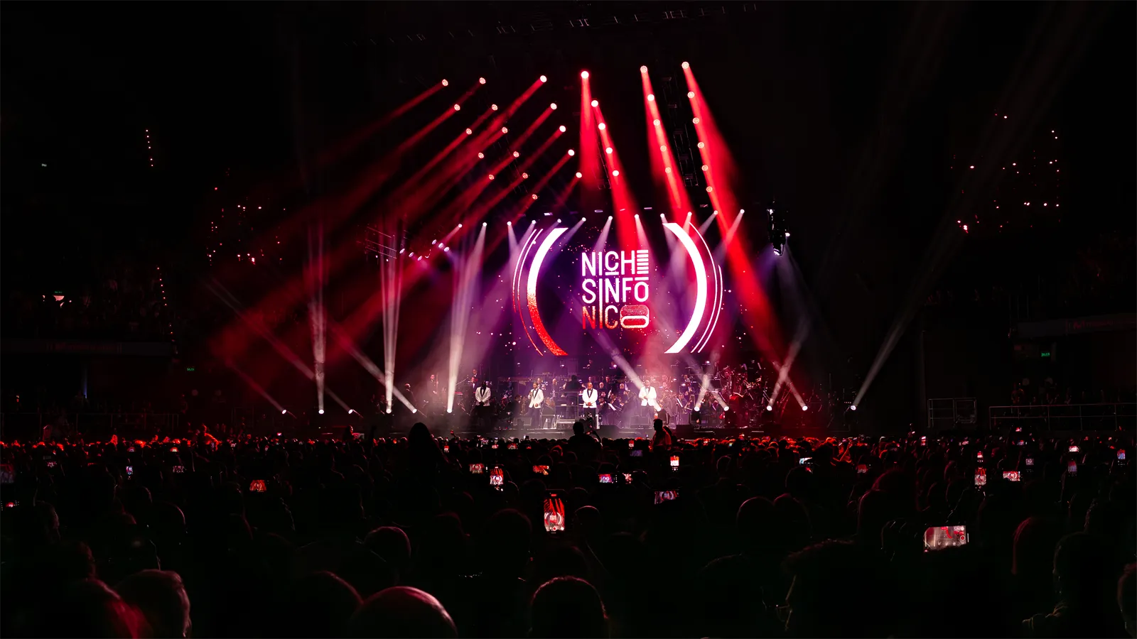 El escenario con el logo de Niche Sinfónico en pantalla y luces rojas sobre el público.