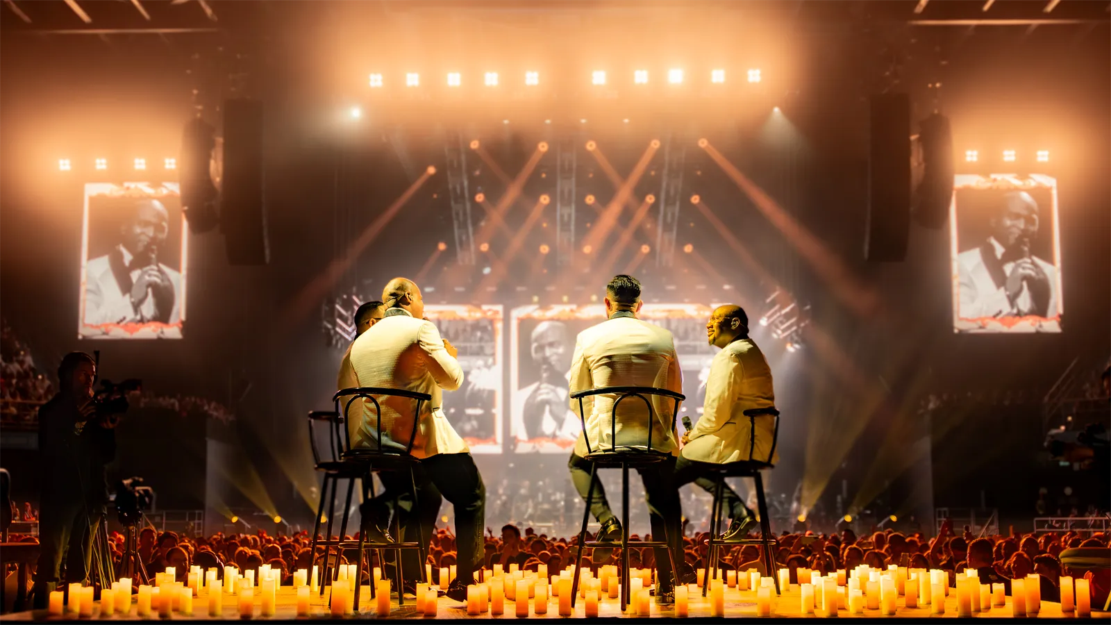 Los cantantes, sentados frente a una hilera de velas, bajo luces cálidas.
