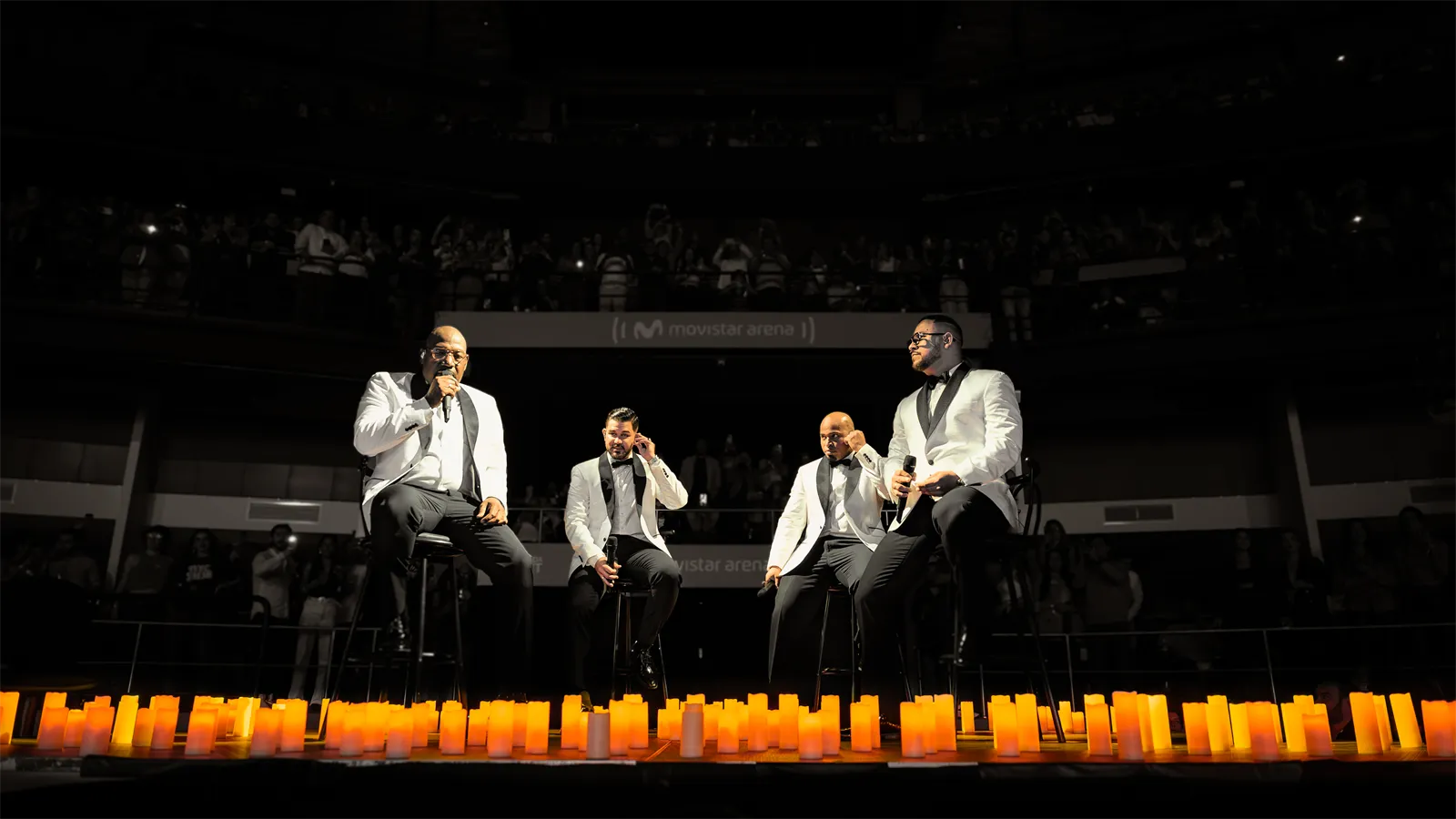 Cuatro cantantes sentados en butacos frente a las velas.