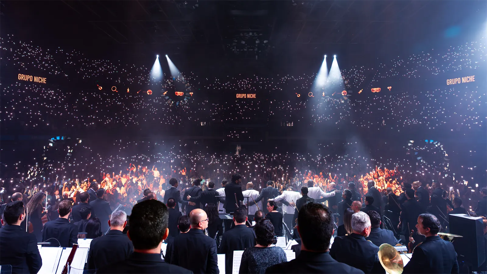 La orquesta frente al público, con luces azules sobre el recinto.