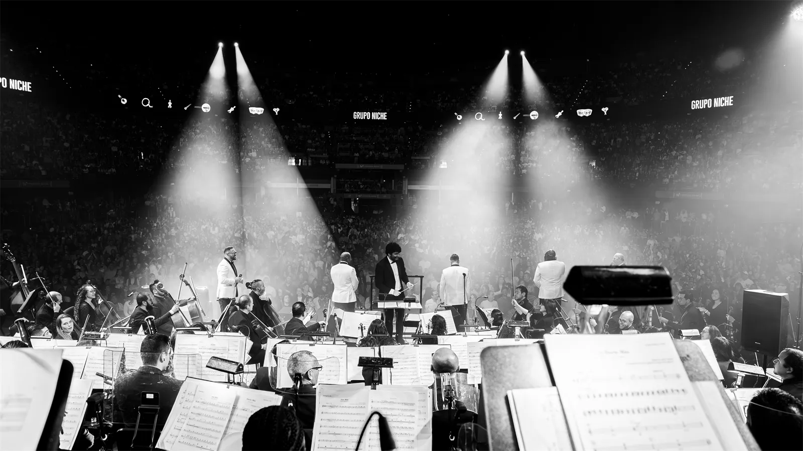 La orquesta y los cantantes bajo los reflectores, en blanco y negro.