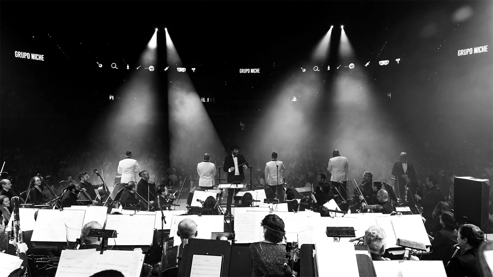 La orquesta y los cantantes bajo los reflectores, en blanco y negro.
