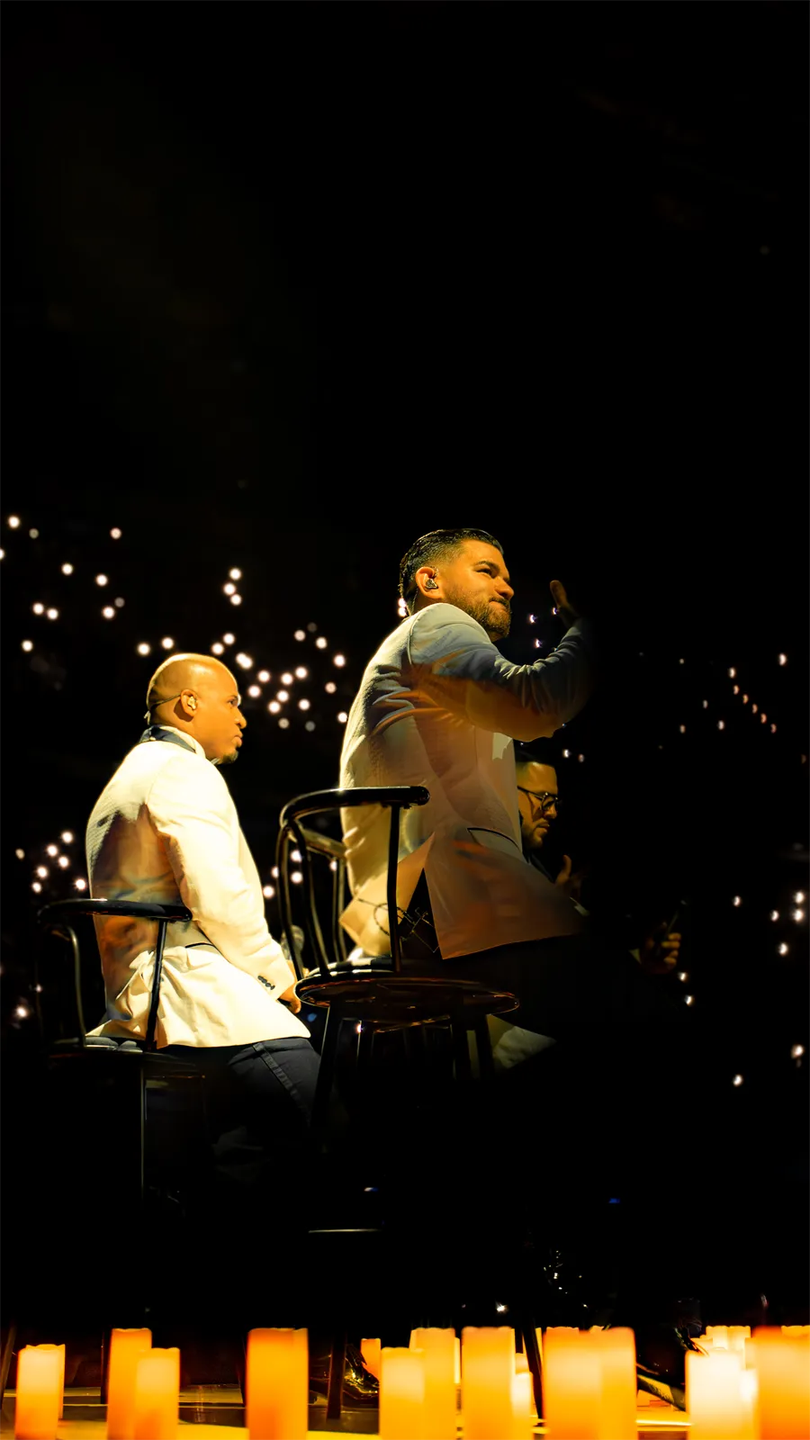 Dos cantantes frente a las velas y las luces de los celulares del público.