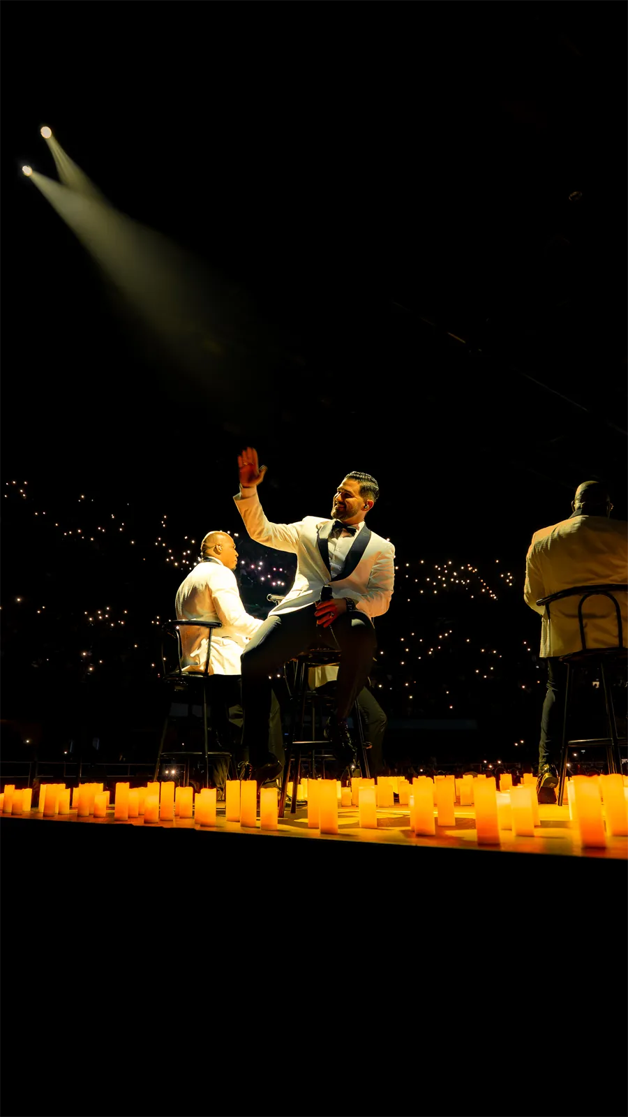 Un cantante levanta la mano en el escenario, frente a las velas.